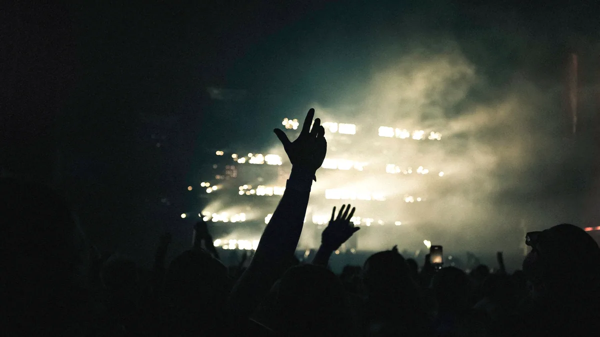 An audience in a dark room with hands in the air.