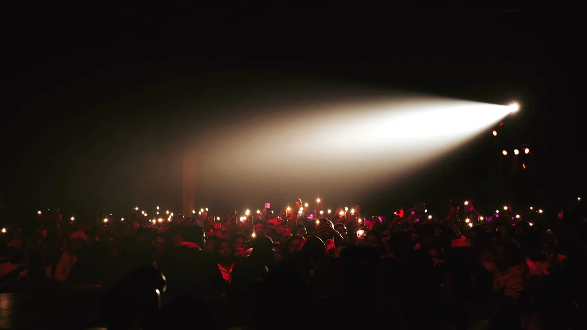 A crowd in a dark room, cheering toward a lit stage.