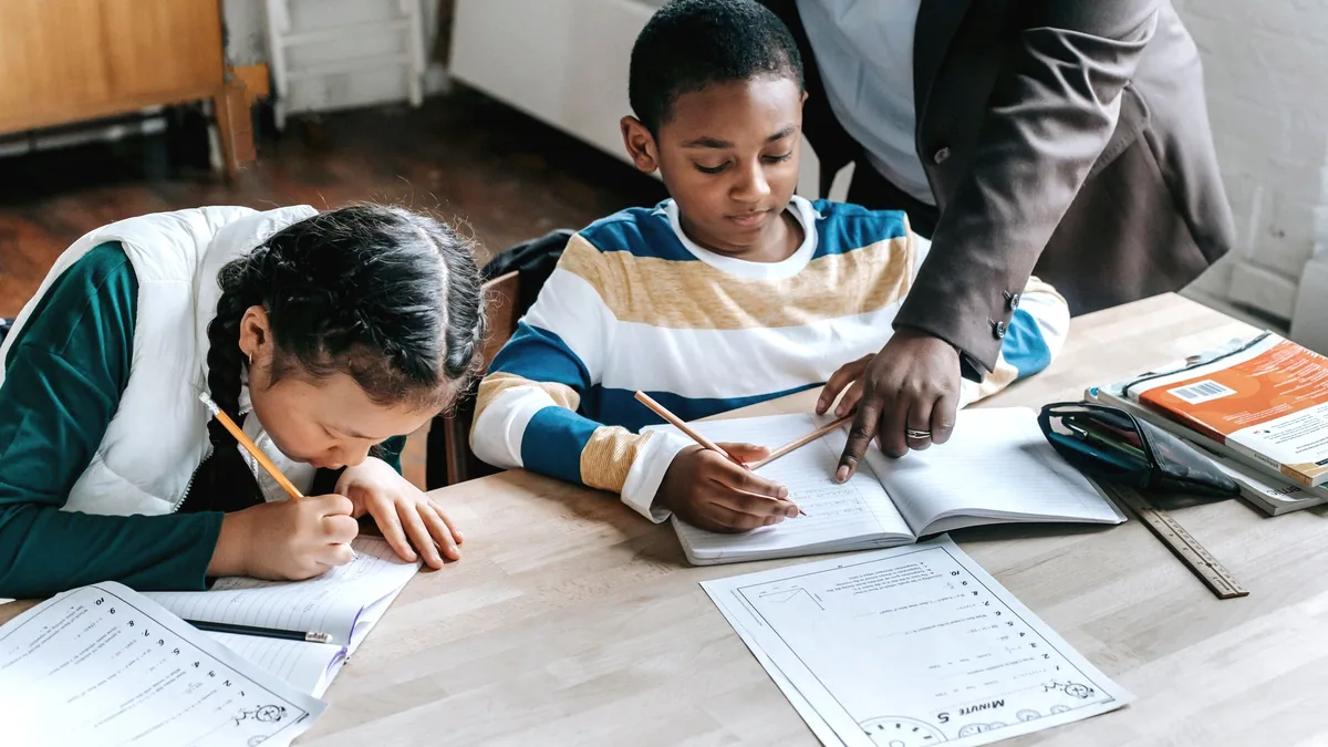 An adult leaning over a desk, working through something with a student.